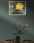 Framed artwork of a yellow flower on a wall above a table with a vase and plants, painting by Kris Horton of a cactus bloom