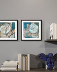 Two framed floral abstract artworks by Kris Horton on a gray wall with books and a decorative figure.