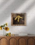 Framed artwork of a red tail hawk's talons by Kris Horton on a white brick wall above a wooden console table with sunflowers.