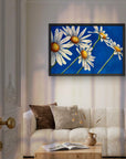 Daisy Days framed painting by Kris Horton of five daisies with blue background over couch.