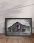 Framed artwork by Kris Horton of a barn with an American flag leaning on a wall.