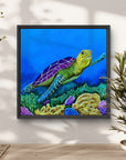Framed artwork by Kris Horton of a turtle on a coral reef against a blue background hanging on a white wall near green plants.