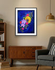 Framed floral painting by Kris Horton on a wall in a living room with a bookshelf and chair.