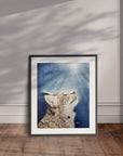Framed artwork by Kris Horton of a bobcat against a blue sky with sunbeams on a wooden floor.