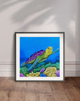 Black framed painting by Kris Horton of Sea of Colors a turtle swimming in blue water over colorful coral displayed leaning against a wall.