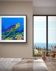 Framed painting by Kris Horton of Sea of Colors a turtle swimming over coral on a wall in a modern bedroom with a view of the ocean.