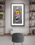 Framed floral cross artwork by Kris Horton on a wall above a desk with shelves and a chair.