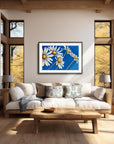 Daisy days black framed painting by Kris Horton above a couch in living room with large windows