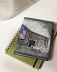 Notebook with a cover featuring a black and white illustration of a barn and truck, with an American flag, painting by Kris Horton