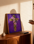 Oak framed He is Risen painting of a rustic cross and flowers propped up on a wooden console with a woman looking at it.