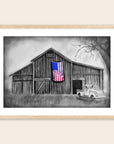Framed artwork by Kris Horton of a barn with an American flag and a pickup truck in front.