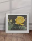 Framed artwork of a yellow cactus flower on a white wall with wooden floor