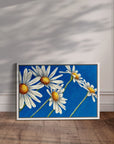 White framed Daisy Days daisy painting by Kris Horton with blue background wall art.