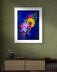 Framed artwork by Kris Horton of colorful flowers on a green wall above a wooden cabinet.