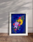 White framed painting by Kris Horton of colorful flowers with a blue background leaning against a wall.