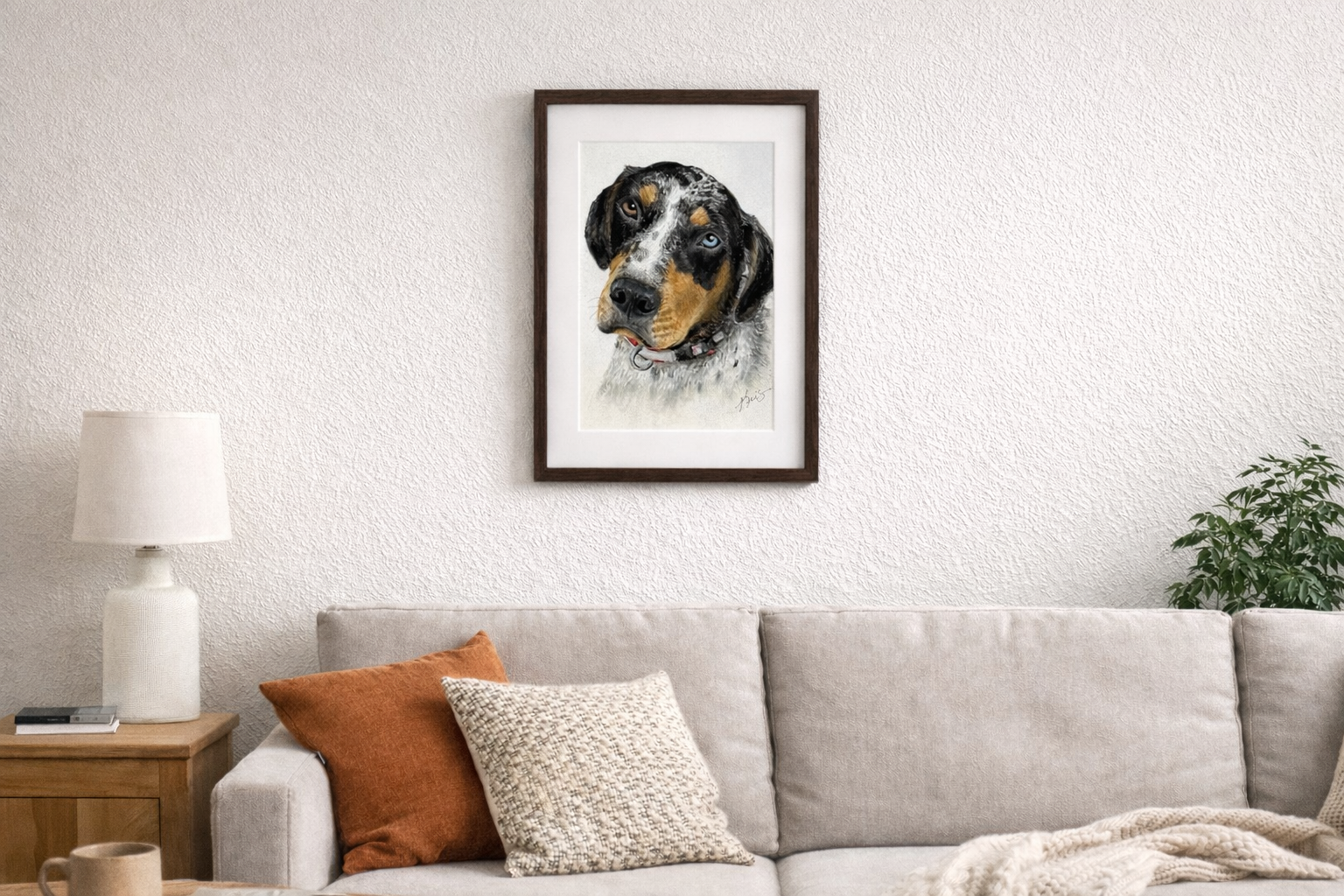 Framed custom pet portrait of a dog created by Kris Horton above a sofa in a living room setting.
