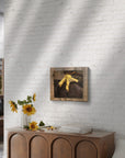 Framed painting of Talon a close up of a red tail hawks foot by Kris Horton, on a white brick wall above a wooden console table with sunflowers.