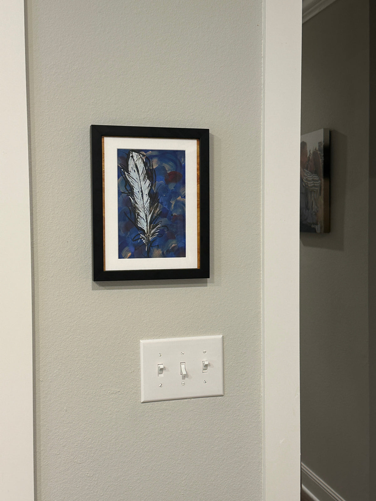 Painting of an abstract feather by Kris Horton hanging on a wall.