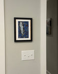 Painting of an abstract feather by Kris Horton hanging on a wall.