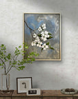 Framed painting by Kris Horton of white flowers on a textured wall above a wooden console table.