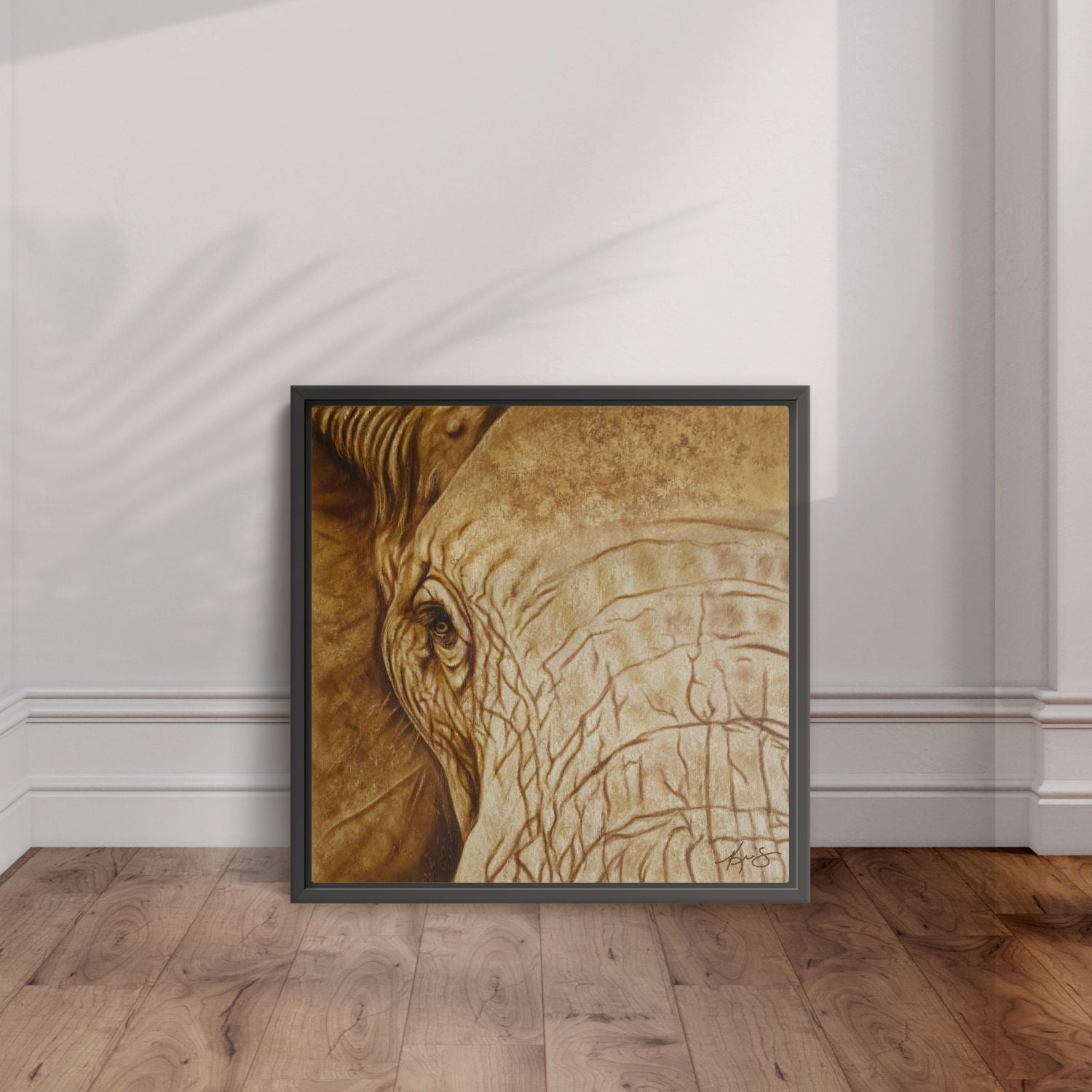 Framed artwork of an elephant's head leaning on a wall with wooden flooring.