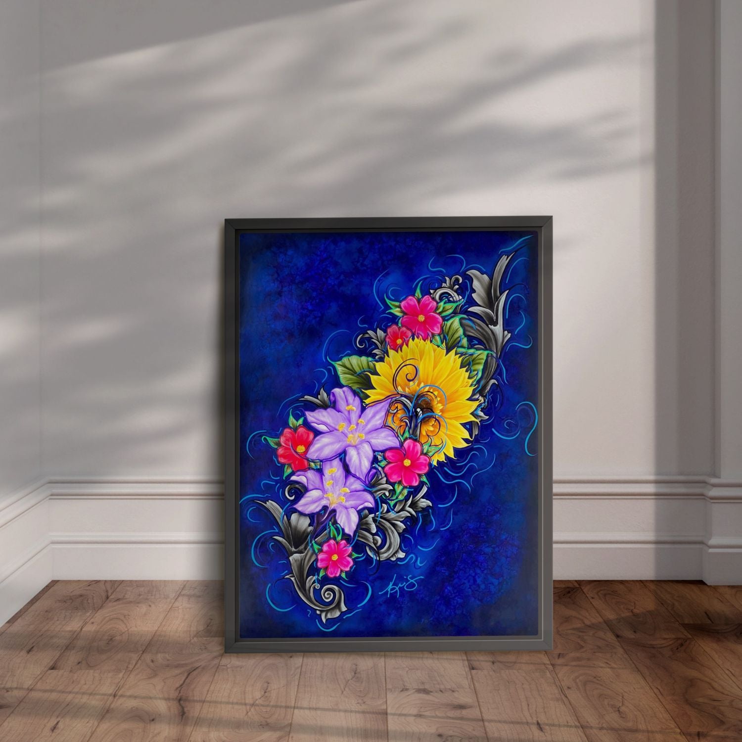 Framed artwork with colorful floral design on a blue background, displayed leaning on a wall.