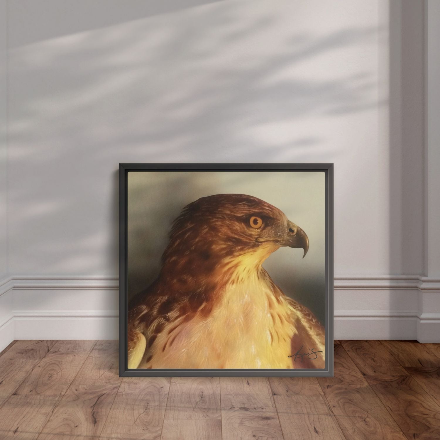Black framed painting of a close up red tail hawk leaning against the wall.