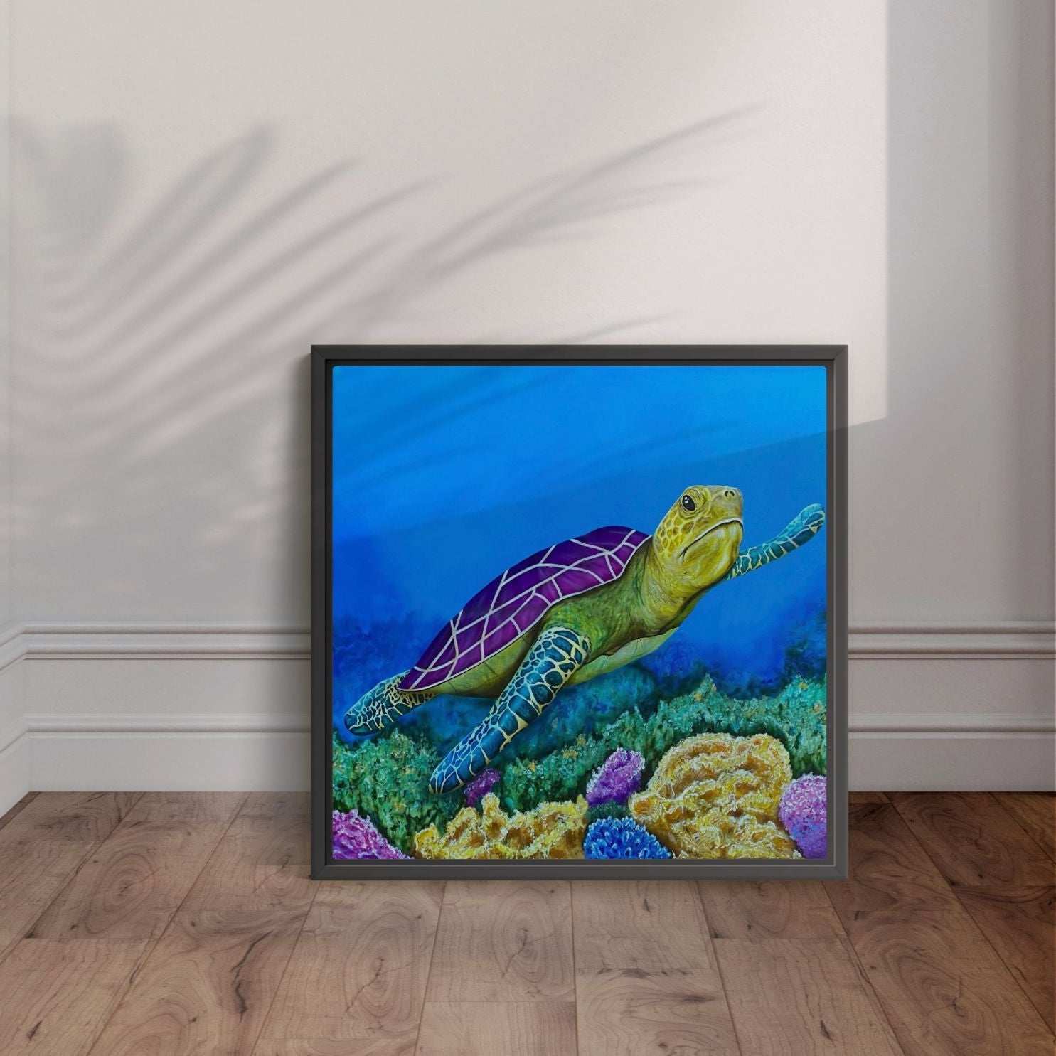 Framed artwork by Kris Horton of a turtle on a coral reef against a blue background, displayed on a wooden floor.