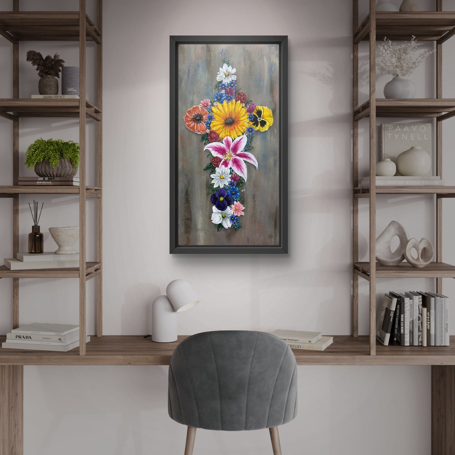 Framed floral painting of a cross made of flower on a wall above a desk with shelves and a chair.