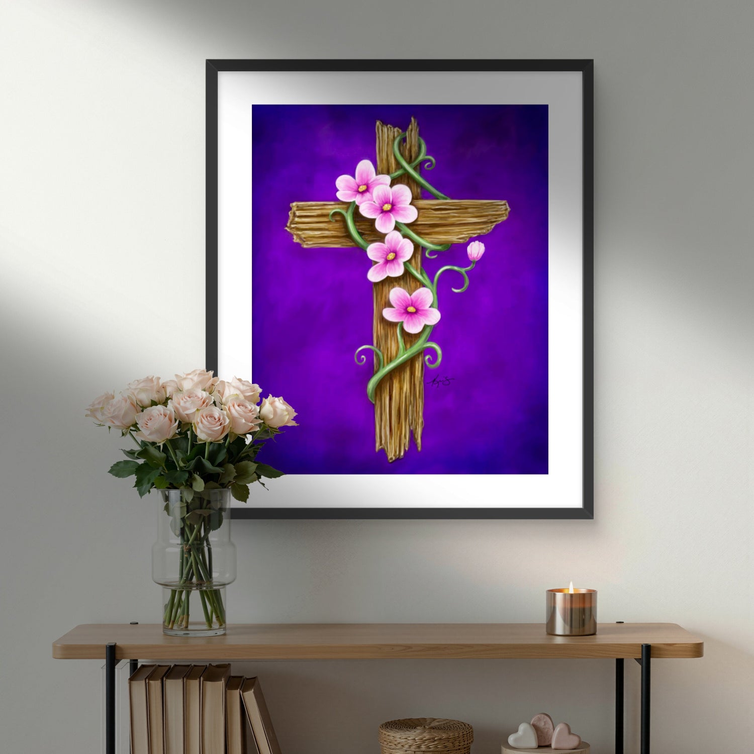 Framed artwork by Kris Horton of He is Risen a cross with flowers on a purple background, displayed above a wooden shelf.