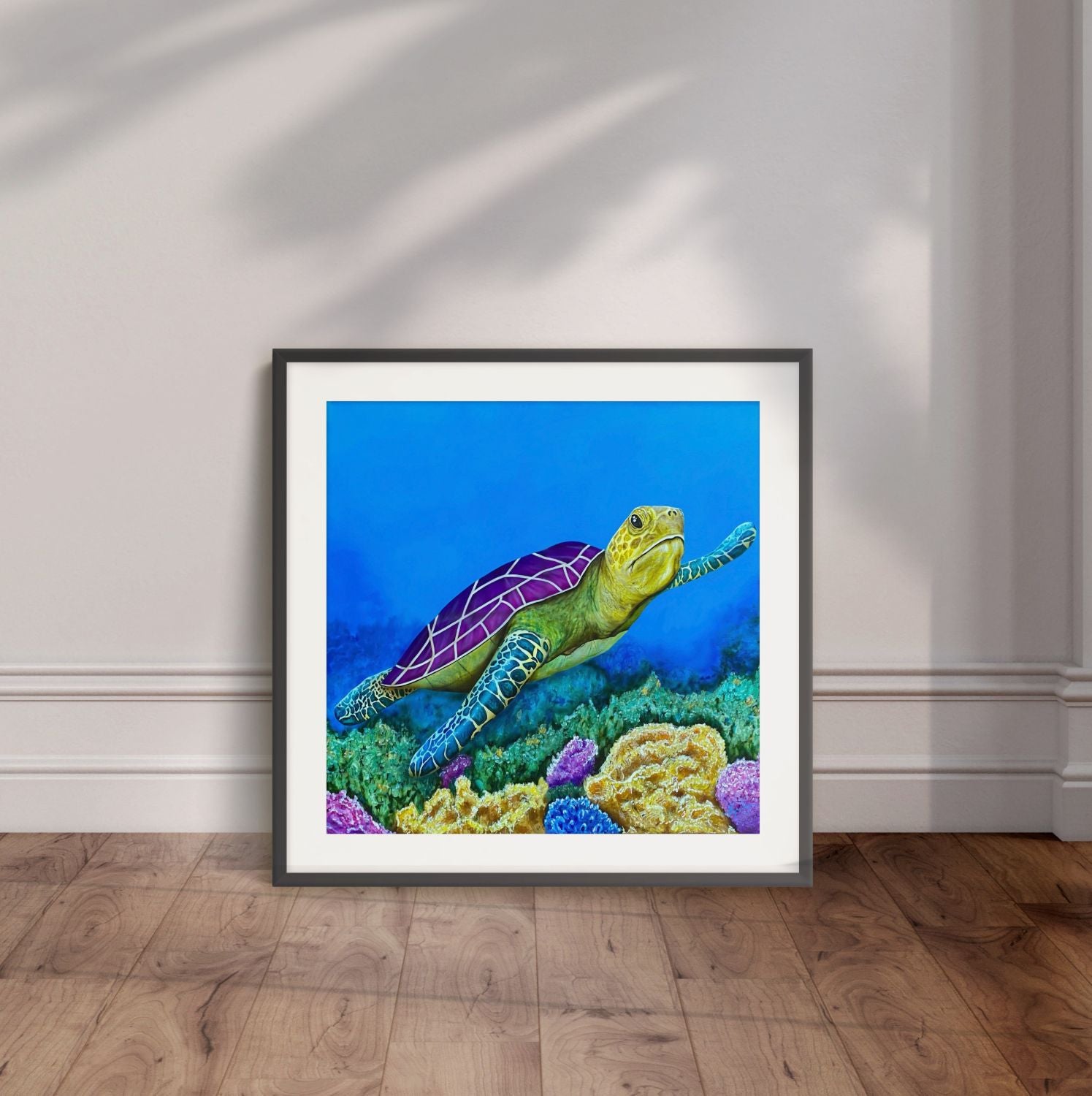 Black framed painting by Kris Horton of Sea of Colors a turtle swimming in blue water over colorful coral displayed leaning against a wall.