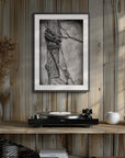 Framed black and white artwork by Kris Horton of Bound which is an old fence post wrapped with barb wire above a turntable on a wooden shelf.