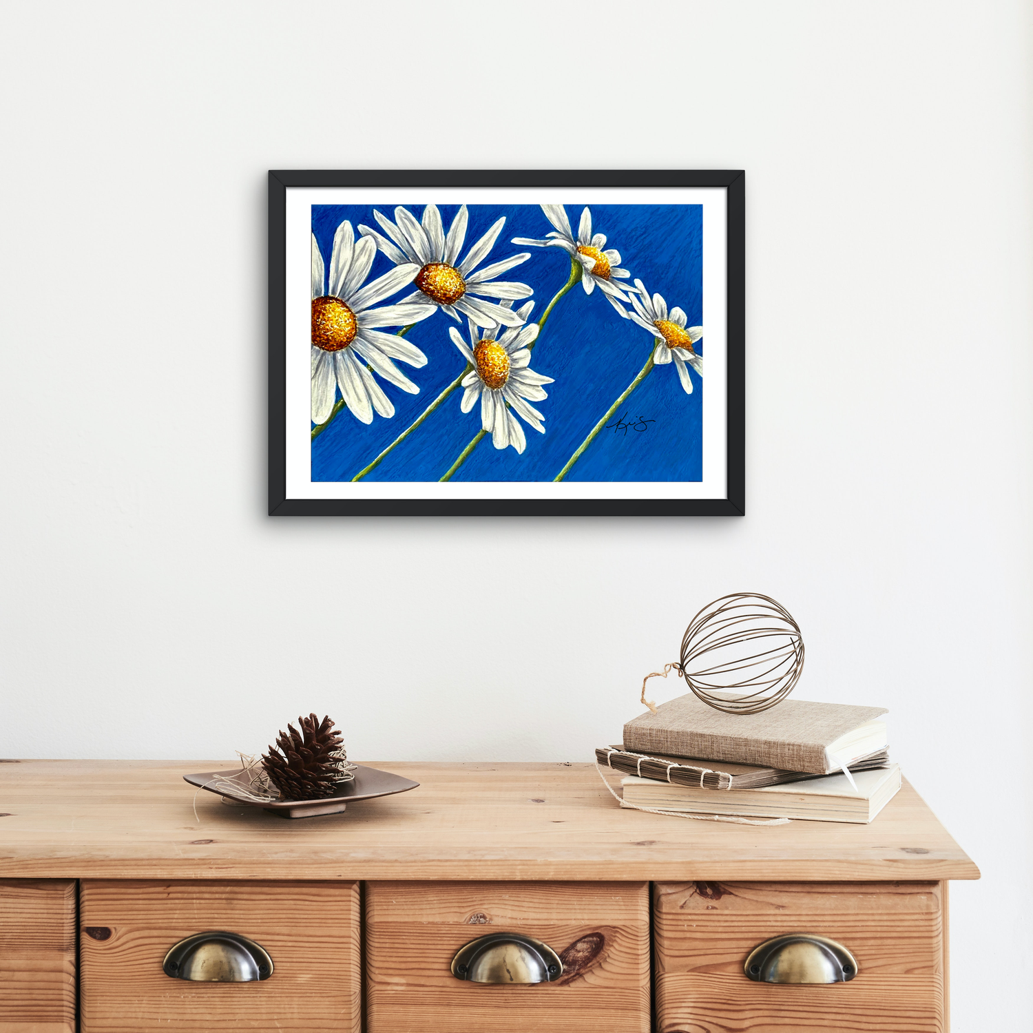 Framed artwork by Kris Horton of Daisy days which is daisies on a blue background above a wooden cabinet.