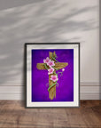 Framed artwork of a wooden cross with pink flowers on a purple background, displayed leaning on a wall.
