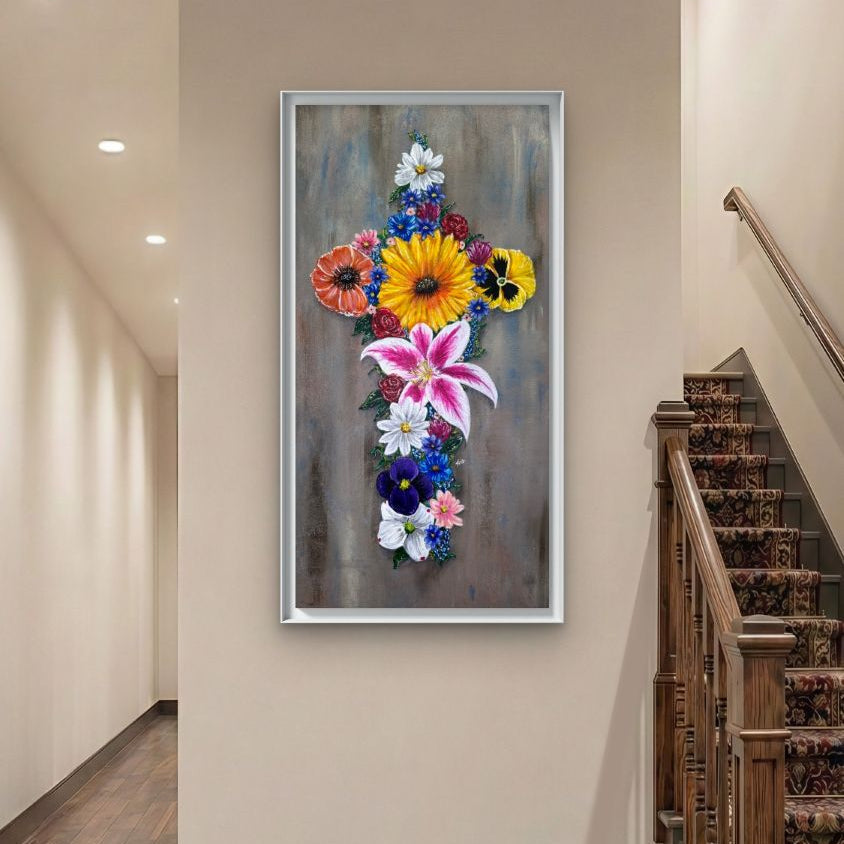 Framed floral artwork by Kris Horton, of a cross made of flowers on a wall next to some stairs.