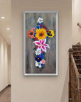 Framed floral artwork by Kris Horton, of a cross made of flowers on a wall next to some stairs.