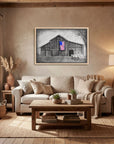 Framed painting of My America by Kris Horton, a monochromatic barn and old truck with an American flag in color hanging in a cozy rustic living room.