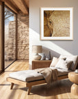 Framed wall art by Kris Horton of an elephant eye painting in sepia in a sunroom with a lounger.