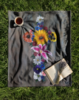 Cross made up of colorful flowers, a painting by Kris Horton printed on a fleece blanket spread out over grass