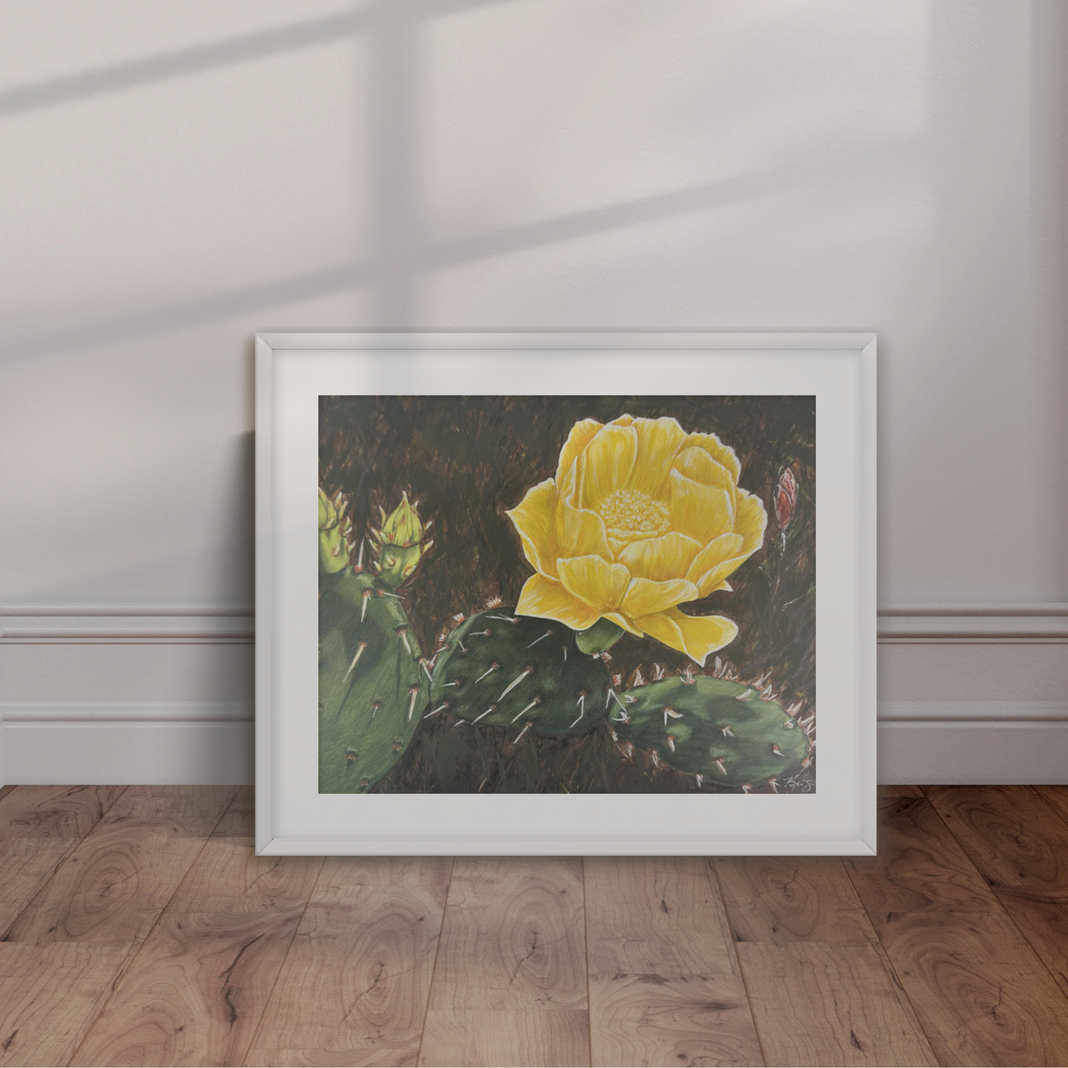 Framed artwork of a yellow cactus flower on a white wall with wooden floor