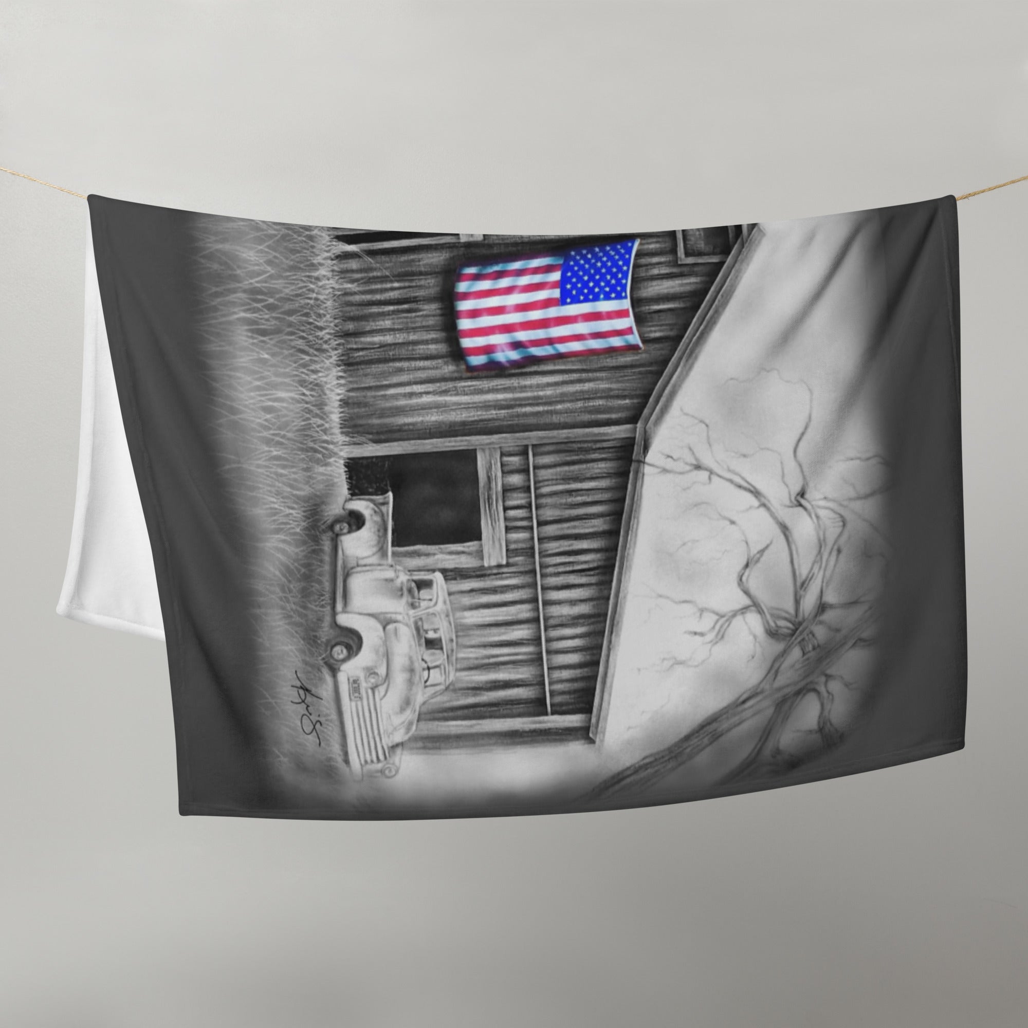 Fleece blanket with black and white painting of a barn and American flag, on a gray background.