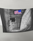 Fleece blanket with black and white painting of a barn and American flag, on a gray background.