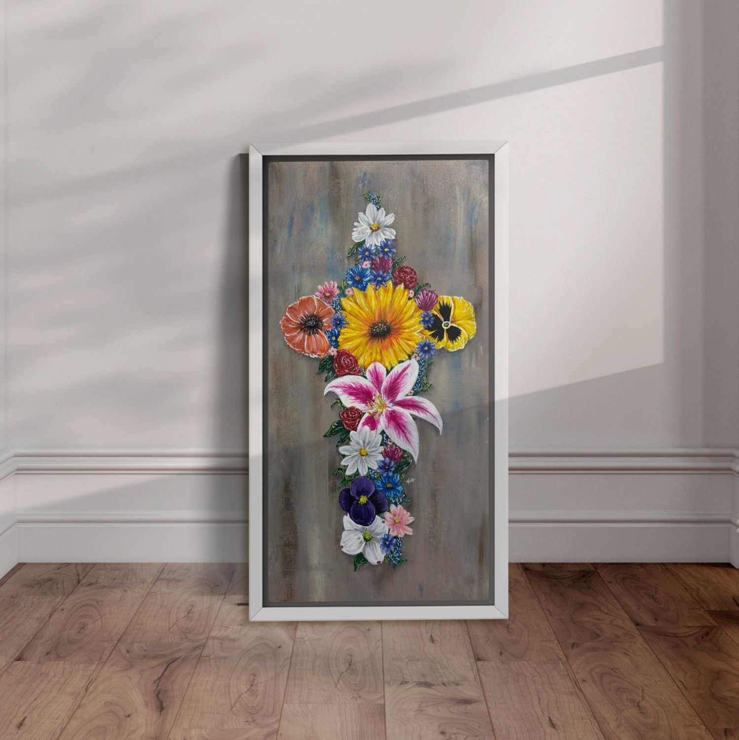 White framed painting of a cross made up of colorful flowers leaning against a wall.