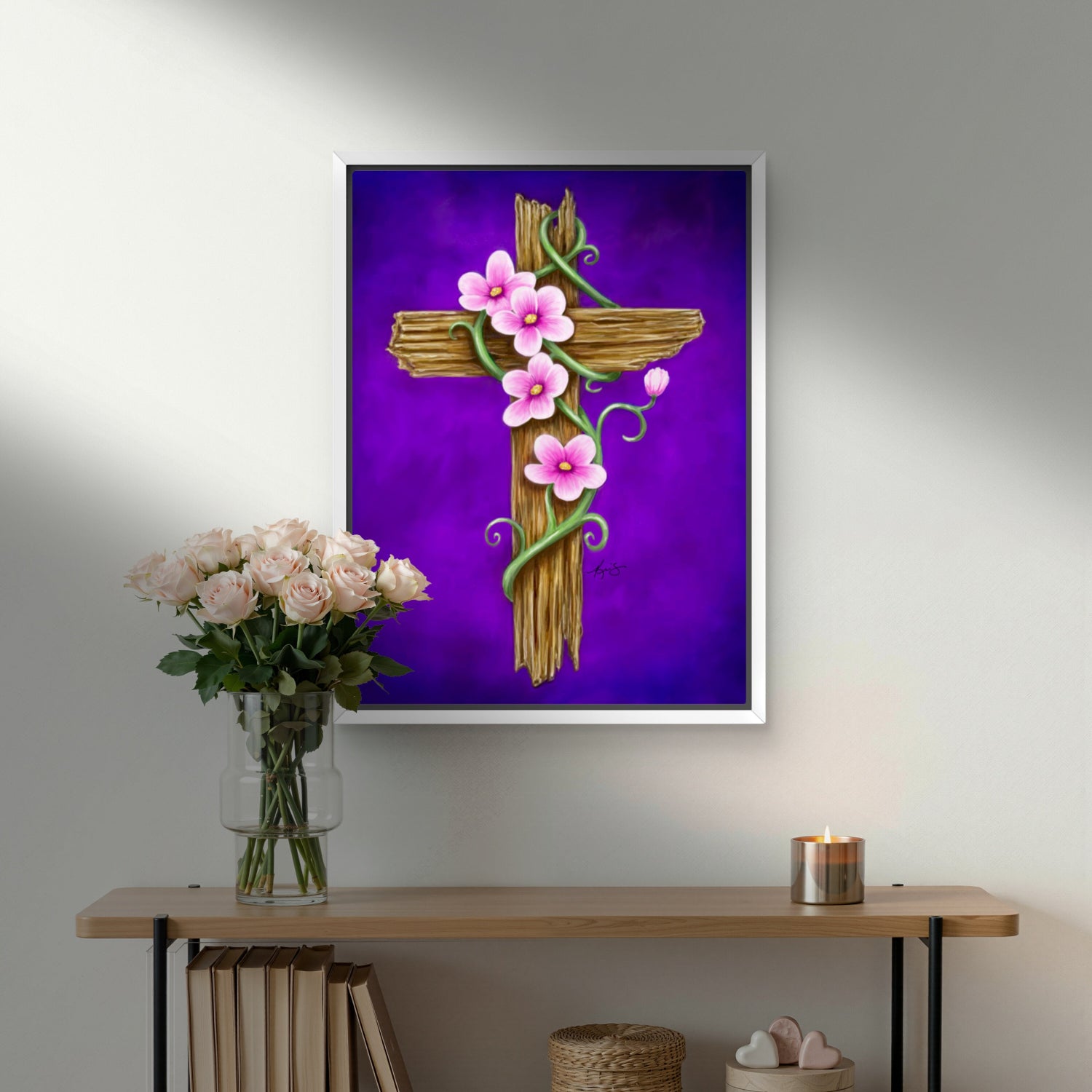 Framed artwork by Kris Horton of a rustic wooden cross with pink flowers on a purple background, displayed above a wooden shelf.