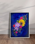 White framed painting of vibrant flowers and blue background by Kris Horton leaning against a wall.