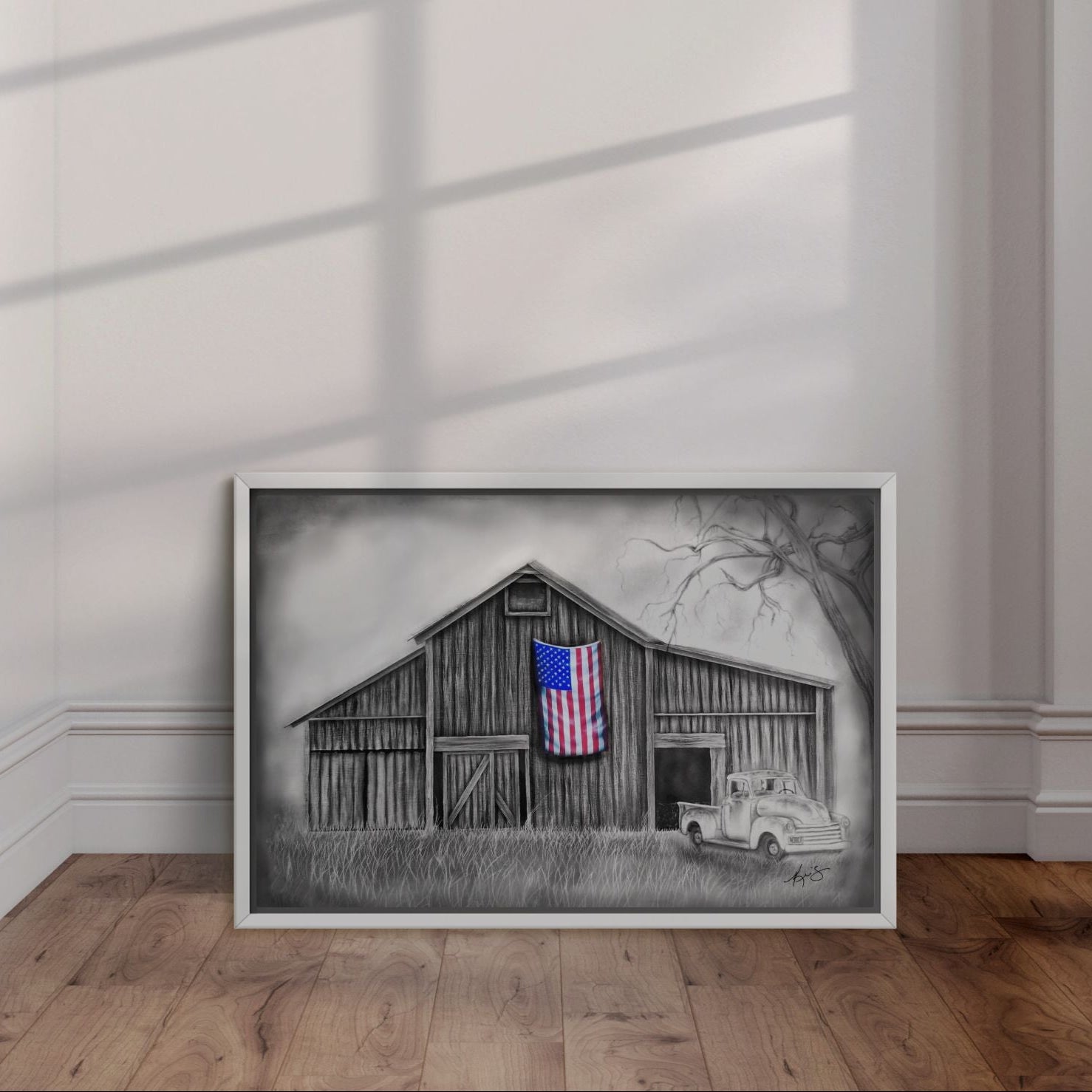 White framed painting by Kris Horton of an old barn and truck with an American Flag leaning against a wall.