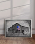 White framed painting by Kris Horton of an old barn and truck with an American Flag leaning against a wall.