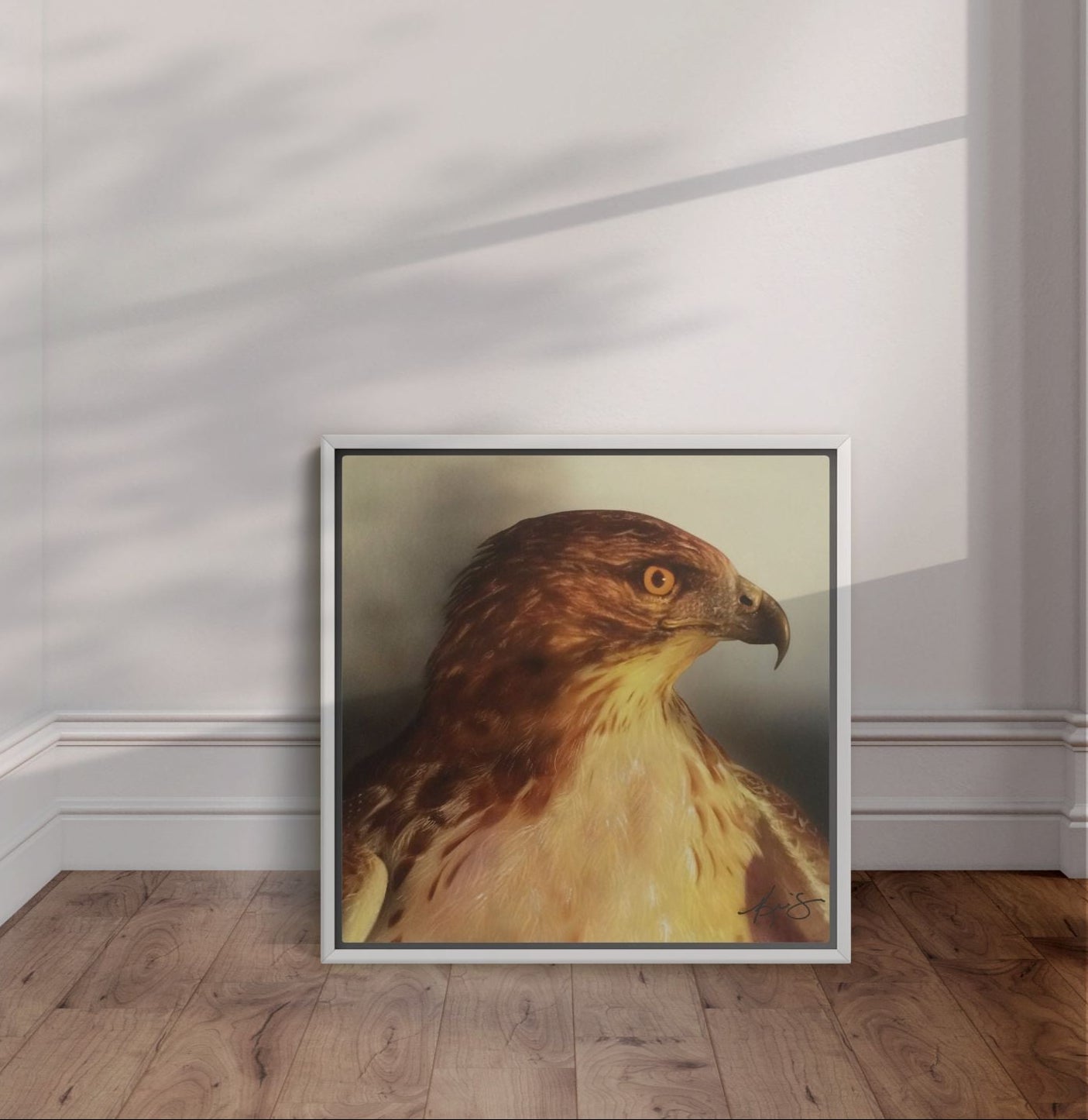 White framed Watchful close up red tail hawk painting leaning against the wall.
