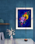 White framed painting of colorful flowers on a blue wall.