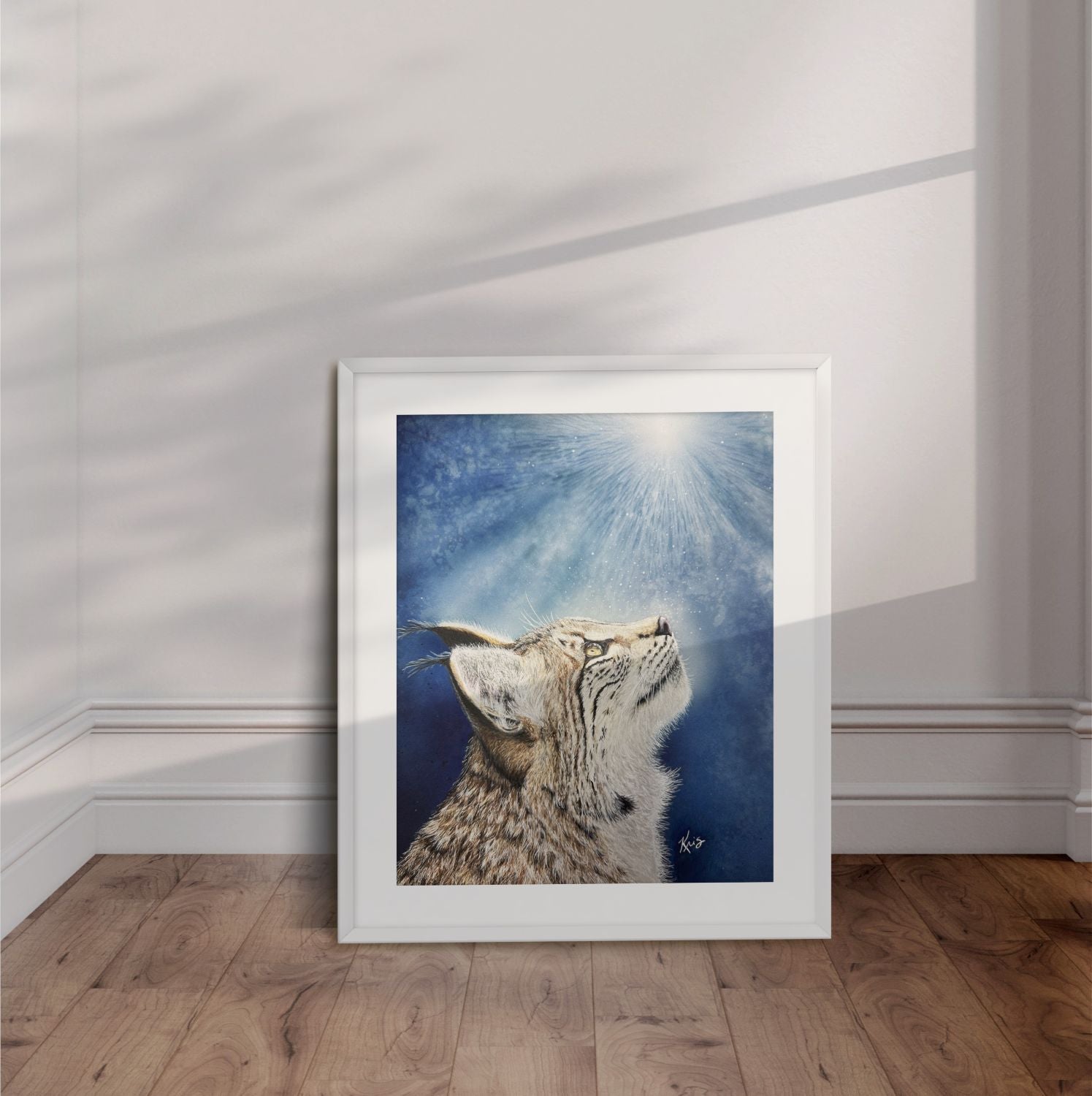 White framed artwork of a bobcat looking up into sunbeams with blue background displayed leaning against the wall.